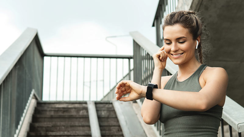Mulher com roupa desportiva consulta o seu smartwatch, numa escada no exterior